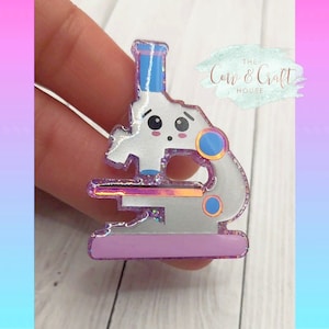 May include: A silver glitter microscope with a pink base and blue accents. The microscope has a cute cartoon face with big eyes. The text "The Corn & Craft House" is visible in the background.