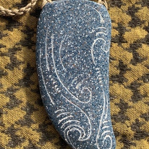 May include: A blue ceramic pendant with a white swirl design, hanging from a brown rope necklace.