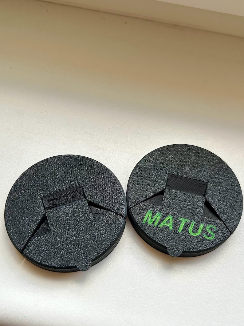 May include: Two black, circular objects with a textured surface. One has the word "MATUS" printed in green. Each object has a rectangular cutout and a triangular section removed, creating a unique shape.