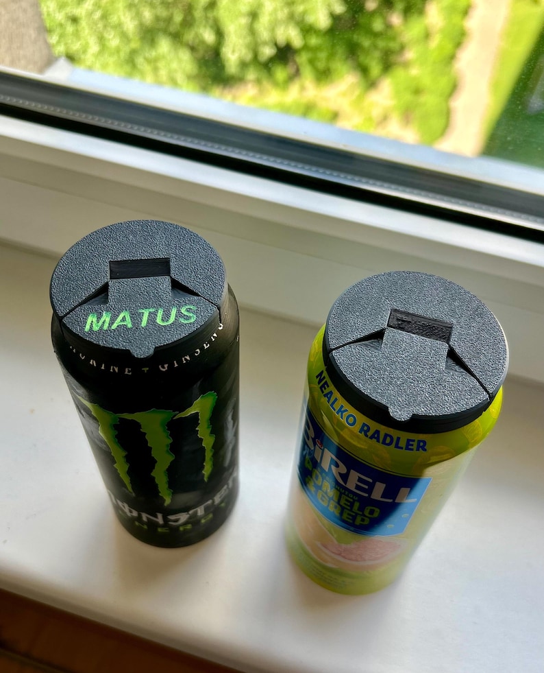 May include: Two aluminum beverage cans with black tops. One can is black with a green logo and the word "MATUS" in green. The other can is yellow and green with the text "SIRELL" and "NEALKO RADLER".