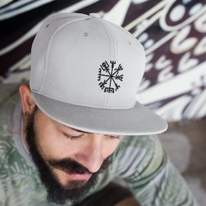 Op de afbeelding: Een grijze en zwarte geborduurde baseballpet met een kompasontwerp en het woord "Vegvisir" in zwart.