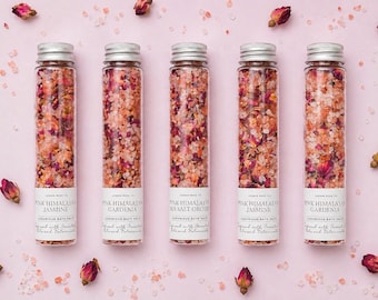 May include: Five glass tubes filled with pink Himalayan bath salts and dried rose petals, with silver caps. The tubes are labeled with the scents: Jasmine, Gardenia, and Sea Salt Orchid. Scattered rose buds and salt crystals on a pink surface.
