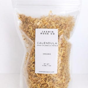 May include: A clear plastic bag filled with dried calendula petals. A white label displays "JASMIN ROSE CO" and "CALENDULA DRIED CALENDULA PETALS ORGANIC" with a net weight of 11.340 / 1 OZ. The website JASMINROSECO.COM is also visible.