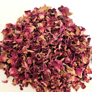 May include: A pile of dried rose petals in shades of pink, red, and tan. The petals are of varying sizes and textures, with some appearing more delicate and others more robust. The background is a plain white surface.