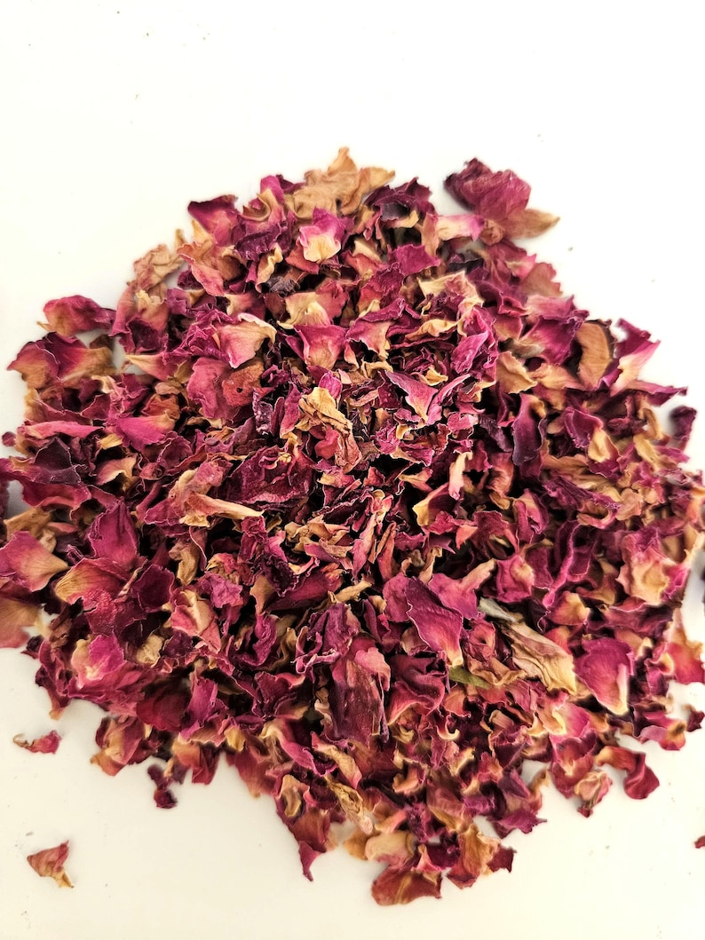 May include: A pile of dried rose petals in shades of pink, red, and tan. The petals are of varying sizes and textures, with some appearing more delicate and others more robust. The background is a plain white surface.