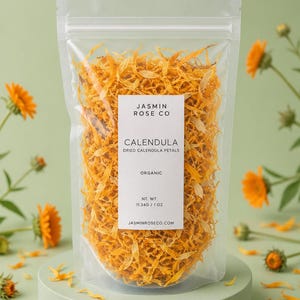 May include: A clear resealable pouch filled with bright orange dried calendula petals. The white label reads JASMIN ROSE CO, CALENDULA, DRIED CALENDULA PETALS, ORGANIC, NT. WT. 11.34G / 1 OZ, and JASMINROSE.COM. The pouch sits on a round green base.