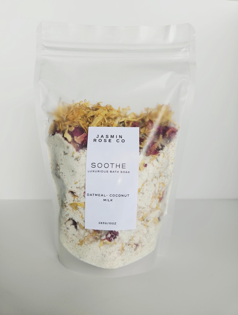 May include: A clear plastic bag filled with a white bath soak, dried flowers, and rose petals. The label reads "JASMIN ROSE CO" and "SOOTHE Luxurious Bath Soak, Oatmeal-Coconut Milk". The bag contains 10 oz of product.