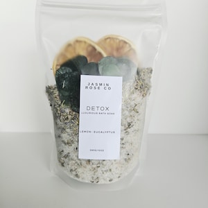 May include: A clear, resealable bag filled with bath soak. The bag contains dried lemon slices, green leaves, and a mix of salts and herbs. A white label reads "JASMIN ROSE CO DETOX LUXURIOUS BATH SOAK LEMON - EUCALYPTUS".