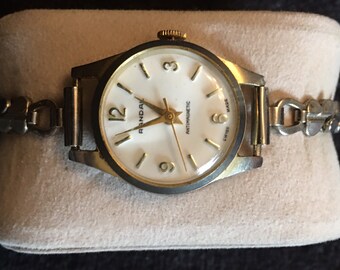 May include: A gold-toned wristwatch with a white face and black hands. The watch has a gold-toned metal band and says "Randal" and "Antimagnetic" on the face.