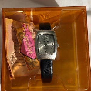 May include: A silver Mudd quartz watch with a black leather band, displayed in an orange plastic case. The watch face has the number 12 at the top and the Mudd logo. The watch is new with a pink tag that says "Stressin' Time Mudd".