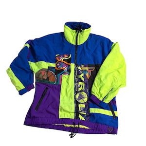 May include: A color-blocked windbreaker jacket featuring a high collar, long sleeves, and a front zipper closure. The design incorporates vibrant blue, neon yellow, and purple panels with graphic prints including the text TYROLIA SONIC FUSION.