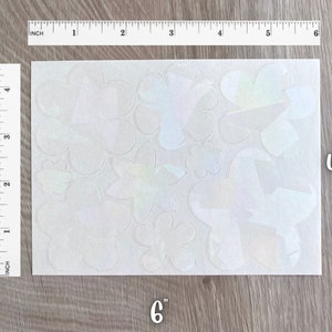 May include: A sheet of iridescent vinyl stickers featuring various flower shapes. The sheet measures 6 inches by 4.5 inches.