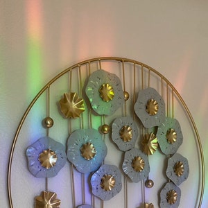May include: A gold metal wall decor with a circular frame and a design of white and gold flowers. The flowers are arranged in a cascading pattern and have a textured surface.