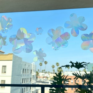 May include: A window with a view of a city skyline and palm trees.  The window is decorated with iridescent flower stickers.