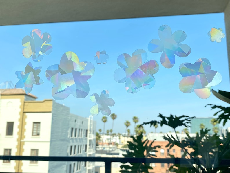 May include: A window with a view of a city skyline and palm trees.  The window is decorated with iridescent flower stickers.