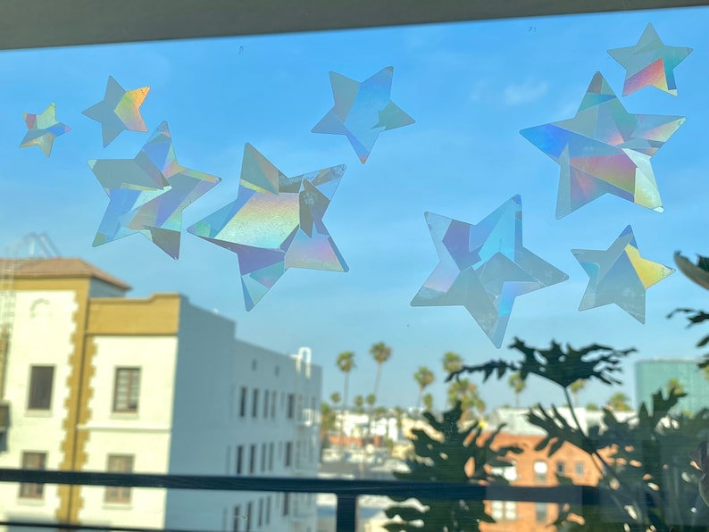 May include: A window with a view of a city skyline and palm trees.  The window is decorated with iridescent star stickers.