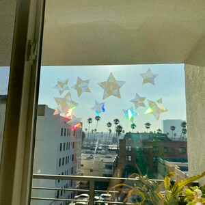 May include: A window with a view of a city skyline. The window is decorated with iridescent star stickers. The stars are arranged in a random pattern.