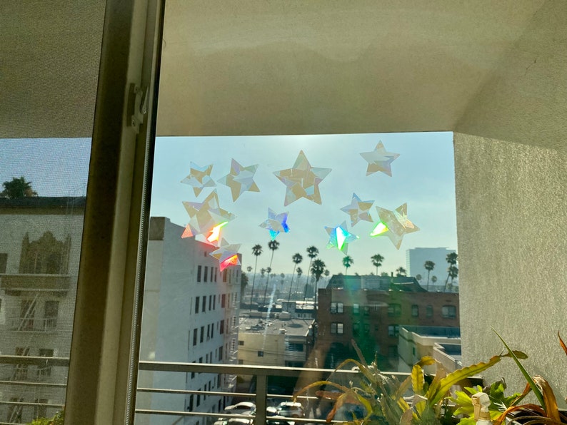 May include: A window with a view of a city skyline. The window is decorated with iridescent star stickers. The stars are arranged in a random pattern.