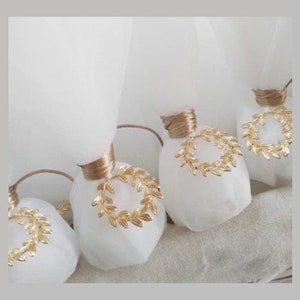 May include: White favor bags with gold leaf wreaths tied with brown ribbon. The bags are filled with small gifts and are perfect for a wedding or other special occasion.