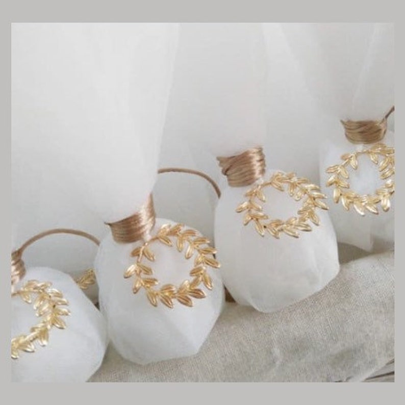 May include: White favor bags with gold leaf wreaths tied with brown ribbon. The bags are filled with small gifts and are perfect for a wedding or other special occasion.