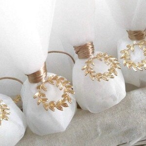 May include: White favor bags with gold ribbon and a gold leaf wreath design. The bags are tied with a gold ribbon and have a gold leaf wreath design on the front.