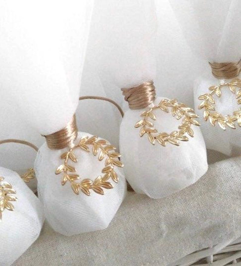 May include: White favor bags with gold ribbon and a gold leaf wreath design. The bags are tied with a gold ribbon and have a gold leaf wreath design on the front.