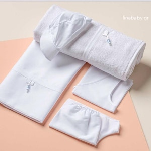May include: A white baby outfit set with a towel, a hat, a onesie, and a diaper. The set is laid out on a light pink surface.