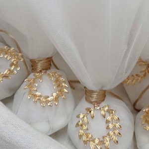 May include: White favor bags with gold laurel wreath designs, tied with a gold ribbon. The bags are made of a sheer fabric and are perfect for a wedding or other special occasion.