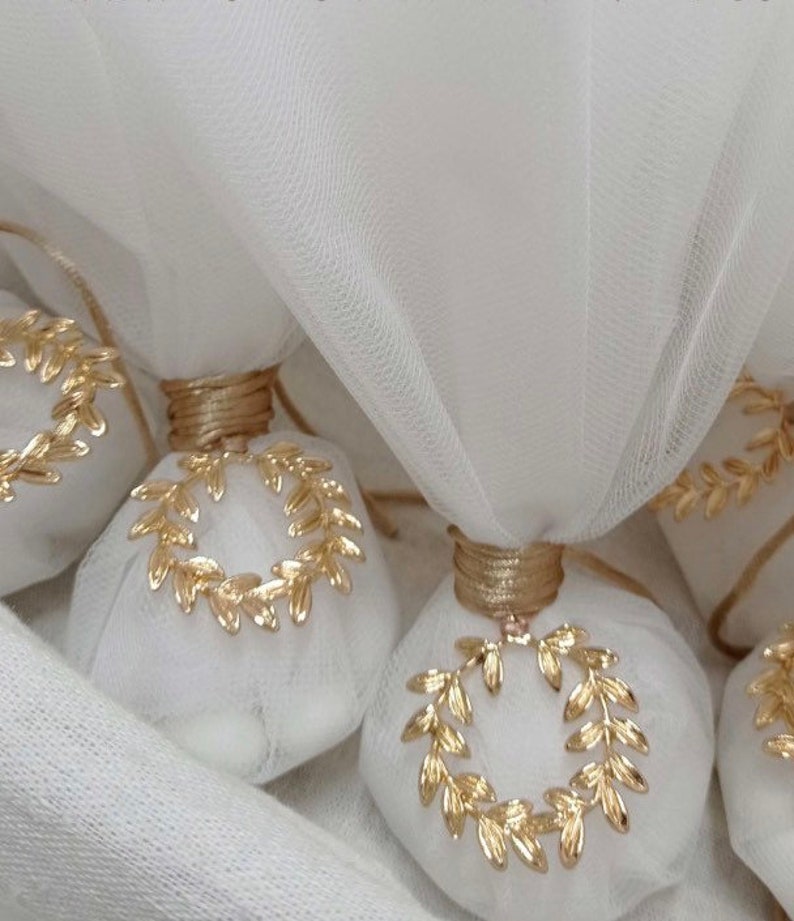 May include: White favor bags with gold laurel wreath designs, tied with a gold ribbon. The bags are made of a sheer fabric and are perfect for a wedding or other special occasion.
