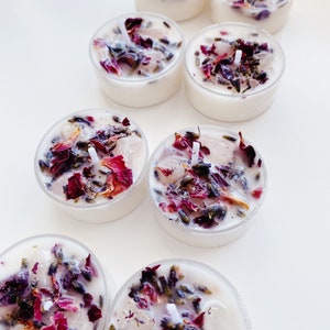May include: A set of eight tealight candles with dried rose petals and lavender buds embedded in the wax. The candles are in clear glass holders.