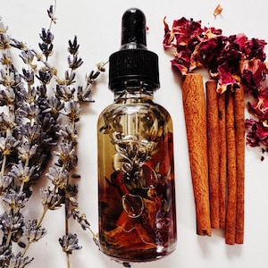 May include: A clear glass dropper bottle filled with a golden liquid, containing dried botanicals. The bottle is flanked by dried lavender sprigs, cinnamon sticks, and red rose petals, all set against a white background. The bottle has a black dropper.