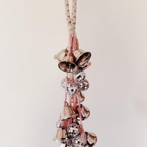 May include: A white and pink macrame string with silver bells and disco ball ornaments hanging from it.