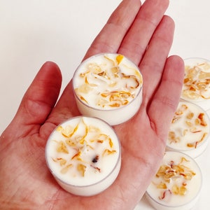 Peut inclure: Un ensemble de quatre bougies chauffe-plat blanches avec des p&eacute;tales de fleurs s&eacute;ch&eacute;es incrust&eacute;s dans la cire. Les bougies sont dans un r&eacute;cipient en plastique transparent.