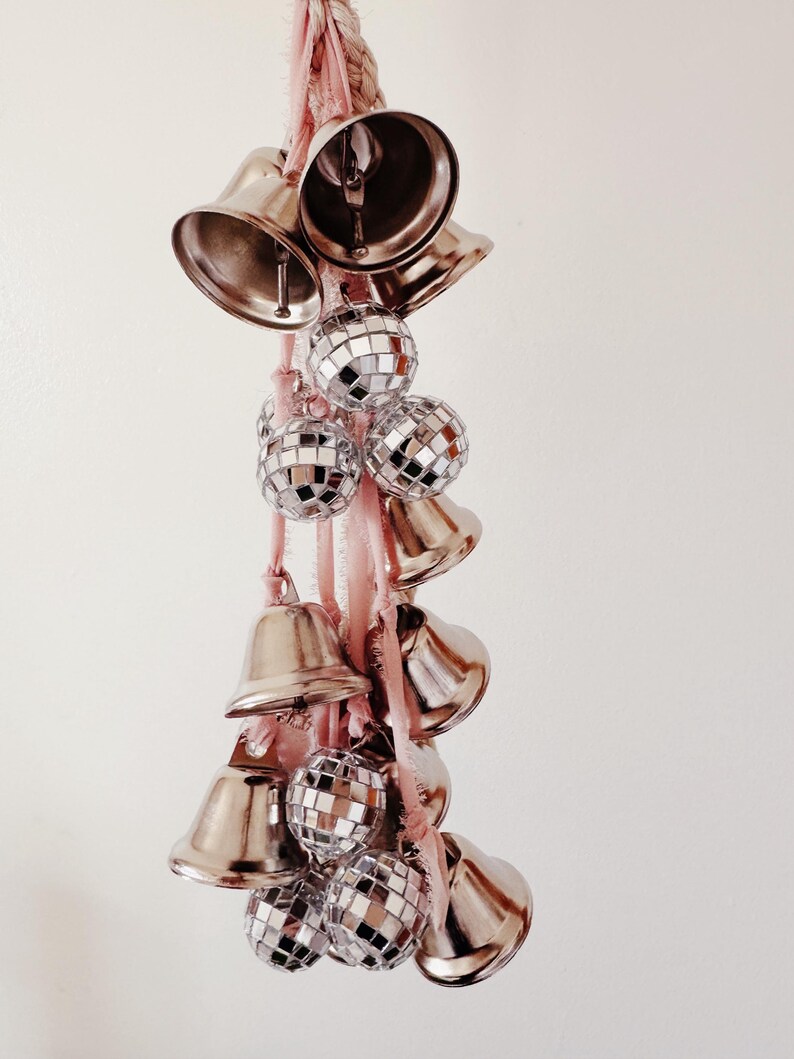 May include: A pink ribbon with silver bells and disco balls hanging from it.