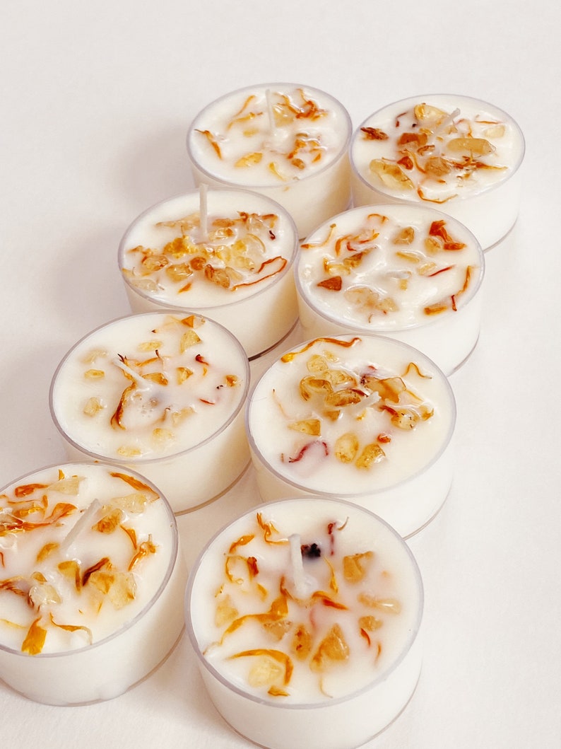 Peut inclure: Huit bougies chauffe-plat blanches avec une cire transparente et des fleurs s&eacute;ch&eacute;es et des cristaux incrust&eacute;s. Les bougies sont dispos&eacute;es en rang&eacute;e sur une surface blanche.