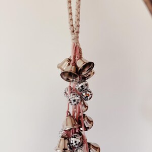 May include: A white rope with a pink tassel hangs from the ceiling. Attached to the tassel are silver bells and silver disco balls.