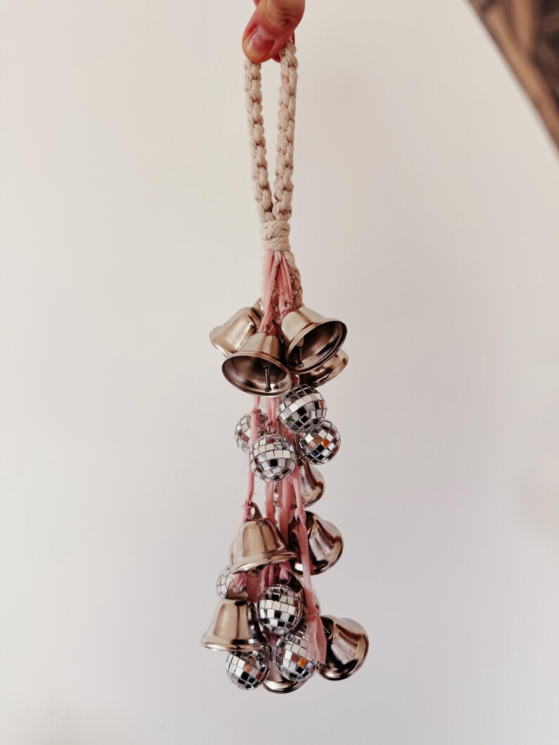May include: A white rope with a pink tassel hangs from the ceiling. Attached to the tassel are silver bells and silver disco balls.