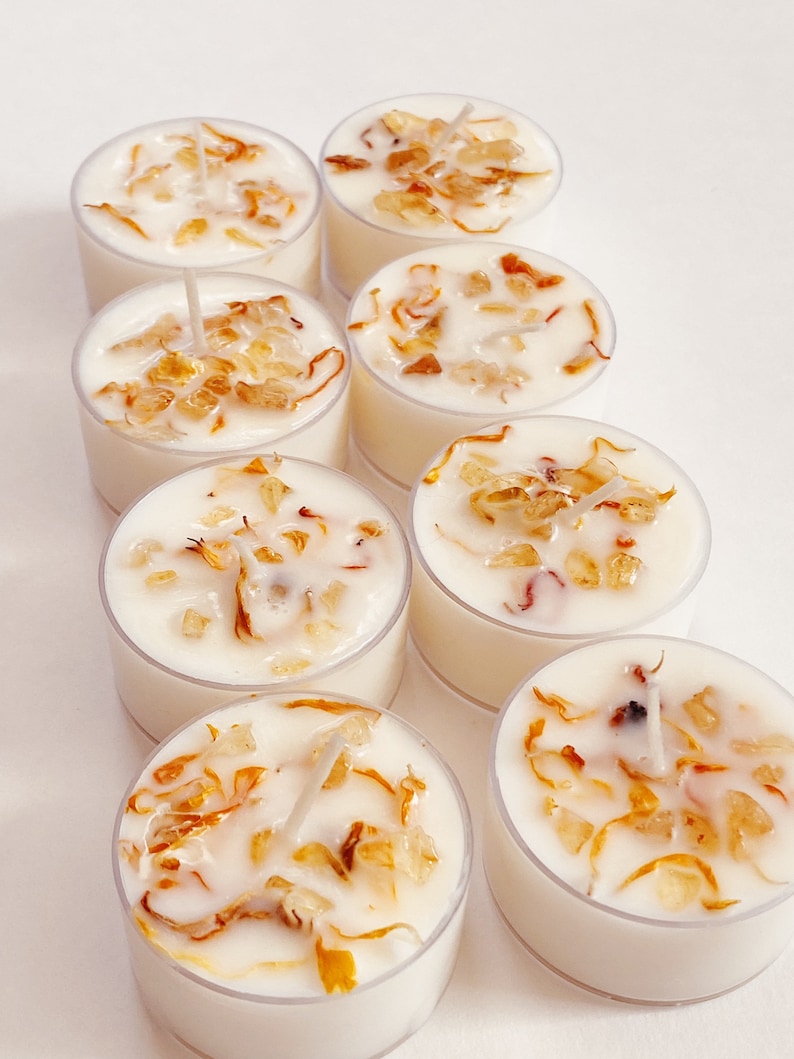 Peut inclure: Un ensemble de huit bougies chauffe-plat blanches avec des p&eacute;tales de fleurs s&eacute;ch&eacute;es incrust&eacute;s dans la cire. Les bougies sont dispos&eacute;es en forme de pyramide sur une surface blanche.