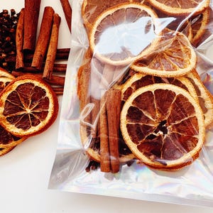 May include: A clear plastic bag filled with dried orange slices, cinnamon sticks, and cloves. The bag is on a white surface.