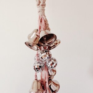 May include: A white rope with pink ribbon and silver bells and disco balls hanging from it.