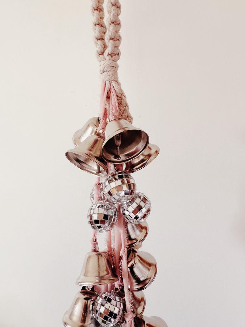 May include: A white rope with pink ribbon and silver bells and disco balls hanging from it.