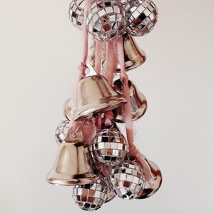 May include: A string of silver bells and disco ball ornaments hanging from a pink and white rope.