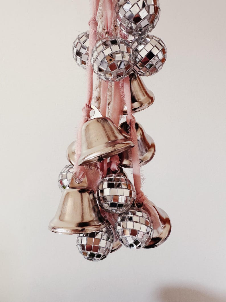 May include: A string of silver bells and disco ball ornaments hanging from a pink and white rope.