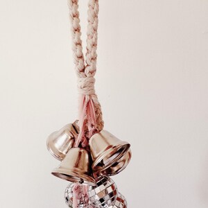 May include: A white rope with a pink tassel hangs from the ceiling. Attached to the rope are a cluster of silver bells and disco ball ornaments.