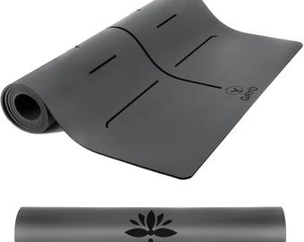 May include: A rolled-up dark gray yoga mat with black alignment lines and the word "GAYO" printed on the mat. The rolled mat shows a black lotus flower design. The mat is designed for yoga and exercise.