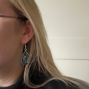 May include: A pair of teardrop-shaped earrings with a silver setting and a dark blue and white marbled design.