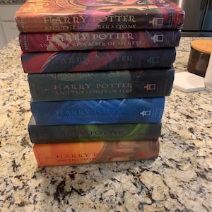Op de afbeelding: Een stapel van zeven boeken uit de Harry Potter-serie. De kleurrijke covers tonen titels als "Harry Potter en de Steen der Wijzen" en "Harry Potter en de Relieken van de Dood". De boeken zijn op elkaar gestapeld.