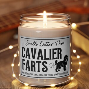 May include: A white candle with a black label that reads "Smells Better Than Cavalier Farts" with a cartoon dog and a fart cloud. The text below the dog reads "Who knew such a small creature could make such a big stink."