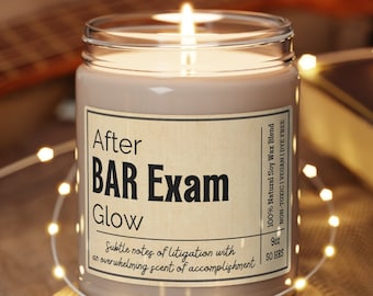 Könnte beinhalten: Eine braune Sojawachskerze mit einem weißen Etikett, auf dem "After BAR Exam Glow" steht. Das Etikett enthält auch den Text "100% Natural Soy Wax Blend", "Non-Toxic | Vegan | Dye Free", "Subtle notes of litigation with an overwhelming scent of accomplishment" und "50 BBS".