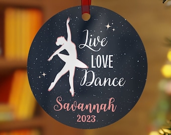 Könnte beinhalten: Ein runder, blauer Weihnachtsbaumschmuck mit einer weißen Silhouette einer tanzenden Ballerina. Der Schmuck hat eine glitzernde Oberfläche und den Text "Live Love Dance" in Weiß mit rosa Umrandung. Der Name "Savannah" und das Jahr "2023" sind ebenfalls in Rosa auf dem Schmuckstück gedruckt.